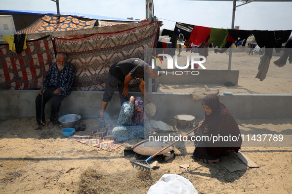 Displaced Palestinians from the eastern part of Khan Yunis are preparing to cook at a temporary camp set up in the grounds of a cemetery in...