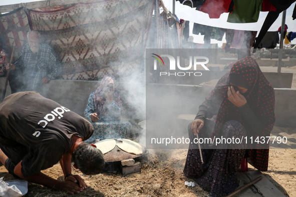 Displaced Palestinians from the eastern part of Khan Yunis are preparing to cook at a temporary camp set up in the grounds of a cemetery in...