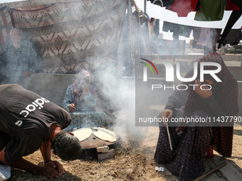 Displaced Palestinians from the eastern part of Khan Yunis are preparing to cook at a temporary camp set up in the grounds of a cemetery in...