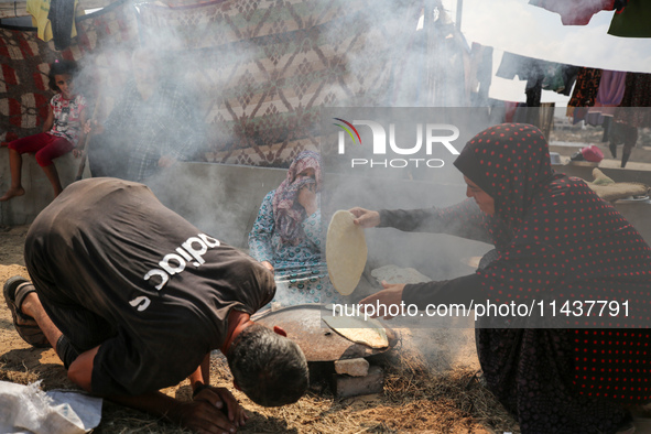 Displaced Palestinians from the eastern part of Khan Yunis are preparing to cook at a temporary camp set up in the grounds of a cemetery in...