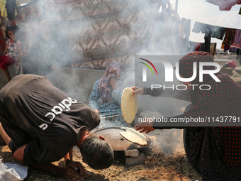 Displaced Palestinians from the eastern part of Khan Yunis are preparing to cook at a temporary camp set up in the grounds of a cemetery in...