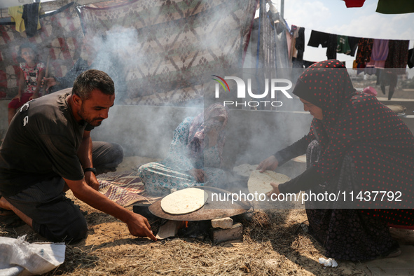 Displaced Palestinians from the eastern part of Khan Yunis are preparing to cook at a temporary camp set up in the grounds of a cemetery in...