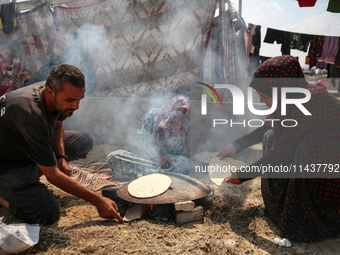 Displaced Palestinians from the eastern part of Khan Yunis are preparing to cook at a temporary camp set up in the grounds of a cemetery in...