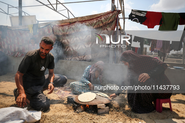 Displaced Palestinians from the eastern part of Khan Yunis are preparing to cook at a temporary camp set up in the grounds of a cemetery in...