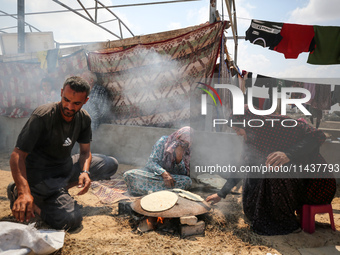 Displaced Palestinians from the eastern part of Khan Yunis are preparing to cook at a temporary camp set up in the grounds of a cemetery in...