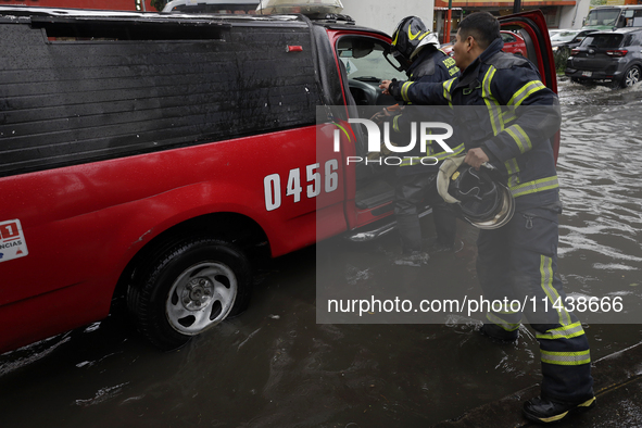 Two firefighters are trying to unclog a drain after flooding is reported in various areas of Mexico City. 