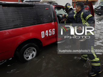 Two firefighters are trying to unclog a drain after flooding is reported in various areas of Mexico City. (