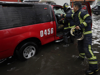 Two firefighters are trying to unclog a drain after flooding is reported in various areas of Mexico City. (