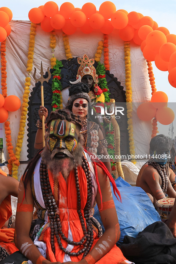 An artist is dressing up as Lord Shiva while kanwariyas are carrying holy water from the shrine 'Galta Peeth Tirtha' and going back to their...