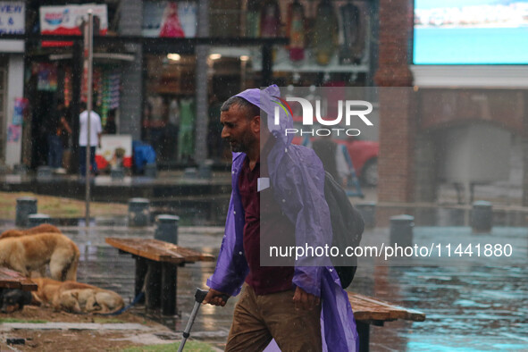 A man is wearing a raincoat and walking along a street as it is raining in Srinagar, Jammu and Kashmir, on July 29, 2024. 