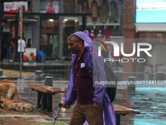 A man is wearing a raincoat and walking along a street as it is raining in Srinagar, Jammu and Kashmir, on July 29, 2024. (