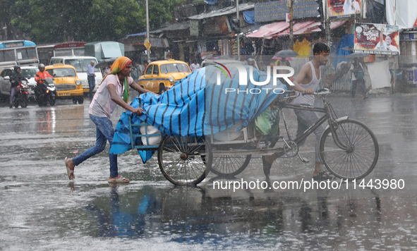 Laborers are transporting a loaded rickshaw with consumer goods to supply a local market on a busy road during monsoon rain, in Kolkata, eas...