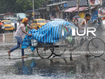 Laborers are transporting a loaded rickshaw with consumer goods to supply a local market on a busy road during monsoon rain, in Kolkata, eas...