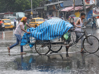 Laborers are transporting a loaded rickshaw with consumer goods to supply a local market on a busy road during monsoon rain, in Kolkata, eas...