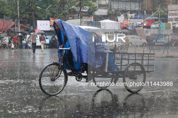 A man is covering himself with a plastic sheet while paddling his rickshaw on a busy road during monsoon rain in Kolkata, India, on July 30,...