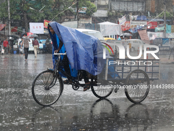 A man is covering himself with a plastic sheet while paddling his rickshaw on a busy road during monsoon rain in Kolkata, India, on July 30,...