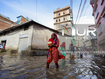 A woman in Nepal is carrying a baby while wading through the flood in Kathmandu, Nepal, on July 6, 2024. (