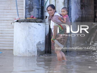 A woman in Nepal is carrying a baby while wading through the flood in Kathmandu, Nepal, on July 6, 2024. (