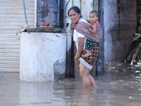 A woman in Nepal is carrying a baby while wading through the flood in Kathmandu, Nepal, on July 6, 2024. (