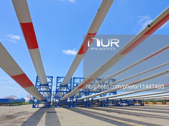 Blades of offshore wind turbines are waiting to be loaded at Penglai Port area of Yantai Port in Yantai, China, on July 31, 2024. On July 31...