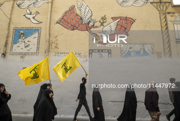 Iranian mourners are walking under a mural while two of them are carrying Lebanon's Hezbollah flag, during a funeral ceremony for Hamas lead...