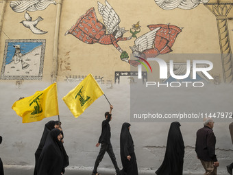 Iranian mourners are walking under a mural while two of them are carrying Lebanon's Hezbollah flag, during a funeral ceremony for Hamas lead...