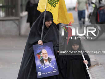 A veiled Iranian woman is carrying a Lebanon's Hezbollah flag and a portrait of Hamas leader Ismail Haniyeh during a funeral ceremony for hi...