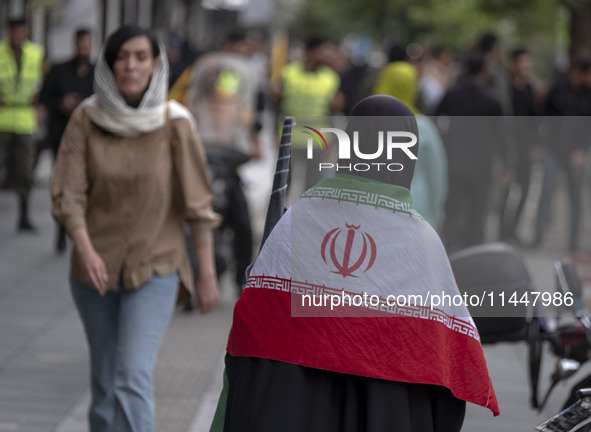 A veiled Iranian woman is wearing an Iranian flag while arriving to participate in a funeral ceremony for Hamas leader Ismail Haniyeh and hi...