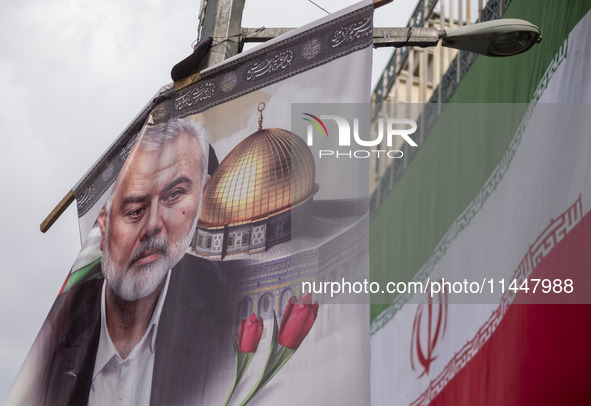 A banner featuring a portrait of Hamas leader Ismail Haniyeh is being hung next to an Iranian flag during a funeral for him and his bodyguar...