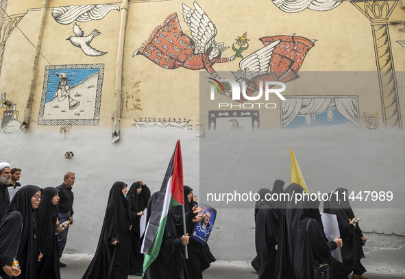 Iranian mourners are walking under a mural while one of them is carrying a Palestinian flag and a portrait of Hamas leader Ismail Haniyeh du...