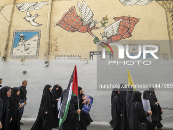 Iranian mourners are walking under a mural while one of them is carrying a Palestinian flag and a portrait of Hamas leader Ismail Haniyeh du...