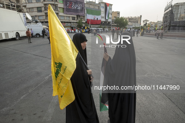 Two veiled Iranian women are holding a Lebanon's Hezbollah flag and a Palestinian flag during a funeral ceremony for Hamas leader Ismail Han...