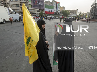 Two veiled Iranian women are holding a Lebanon's Hezbollah flag and a Palestinian flag during a funeral ceremony for Hamas leader Ismail Han...