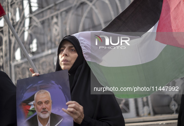 A veiled Iranian woman is sitting next to a Palestinian flag, while she is holding a portrait of Hamas leader Ismail Haniyeh, during a funer...