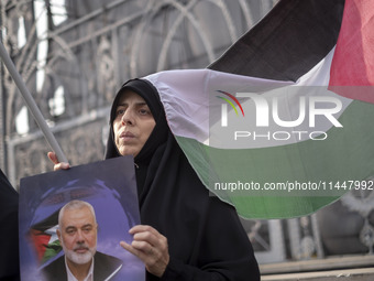 A veiled Iranian woman is sitting next to a Palestinian flag, while she is holding a portrait of Hamas leader Ismail Haniyeh, during a funer...