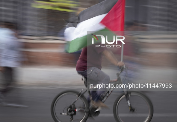 An Iranian man is riding his bicycle along an avenue, while carrying a Palestinian flag, during a funeral ceremony for Hamas leader Ismail H...