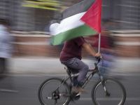 An Iranian man is riding his bicycle along an avenue, while carrying a Palestinian flag, during a funeral ceremony for Hamas leader Ismail H...