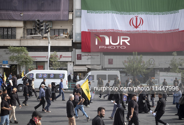 Iranian mourners are walking under a giant Iranian flag while participating in a funeral ceremony for Hamas leader Ismail Haniyeh and his bo...