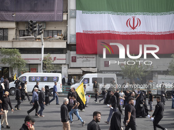 Iranian mourners are walking under a giant Iranian flag while participating in a funeral ceremony for Hamas leader Ismail Haniyeh and his bo...