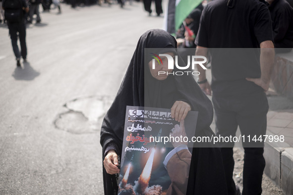 A veiled Iranian woman is carrying an anti-Israeli poster while participating in a funeral ceremony for Hamas leader Ismail Haniyeh and his...