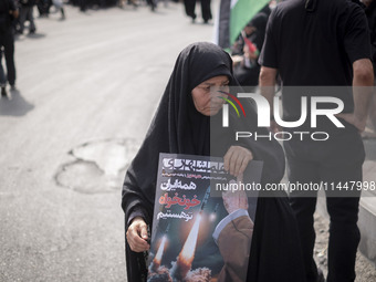 A veiled Iranian woman is carrying an anti-Israeli poster while participating in a funeral ceremony for Hamas leader Ismail Haniyeh and his...