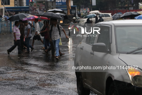 People are crossing a road during monsoon rain in Kolkata, India, on August 1, 2024. 