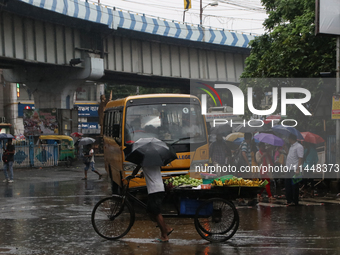 A fruit seller is holding an umbrella while crossing the busy road during monsoon rain in Kolkata, India, on August 1, 2024. (