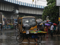 A fruit seller is holding an umbrella while crossing the busy road during monsoon rain in Kolkata, India, on August 1, 2024. (