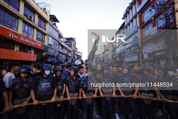 Nepal Police personnel are creating a human barricade, escorting the devotees and the chariot of the Red God, Rato Macchindranath, as it app...