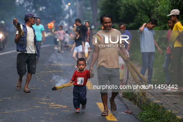 A child is carrying a live hay straw as he walks along with his father during the immolation ceremony of demon deity Ghantakarna to veer off...