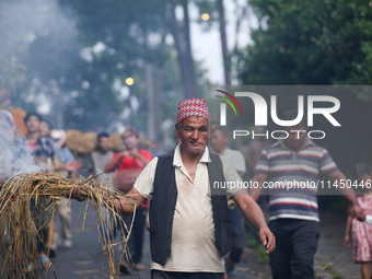 An elderly man is carrying live hay straw as he takes part in the immolation ceremony of the demon deity Ghantakarna to ward off bad omens a...