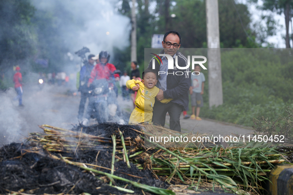 A man is swinging his child over the burning effigy of the demon deity Ghantakarna to veer off bad omens and ward off evil spirits in Bhakta...