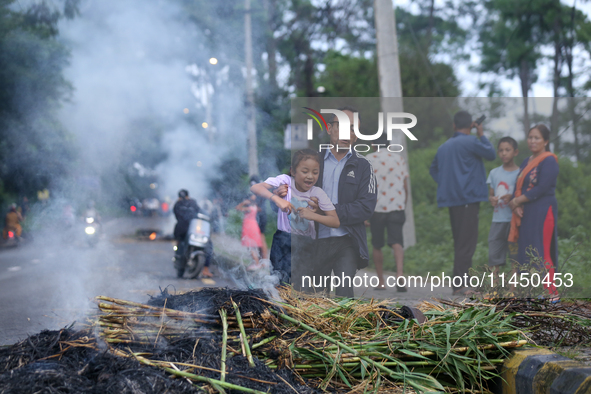 A man is swinging his child over the burning effigy of the demon deity Ghantakarna to veer off bad omens and ward off evil spirits in Bhakta...