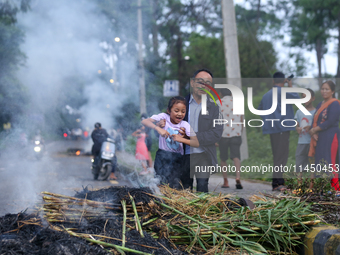 A man is swinging his child over the burning effigy of the demon deity Ghantakarna to veer off bad omens and ward off evil spirits in Bhakta...